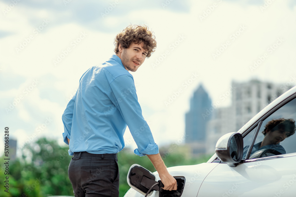 Progressive businessman insert charger plug from charging station to his electric vehicle with apart