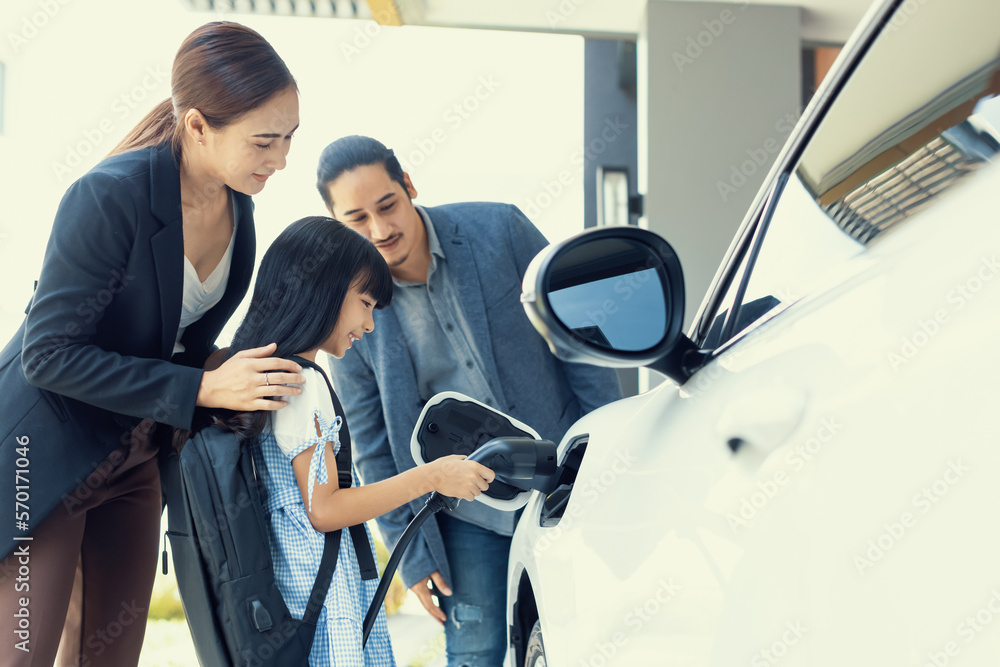 Progressive young parents and daughter with electric vehicle and home charging station. Green and cl