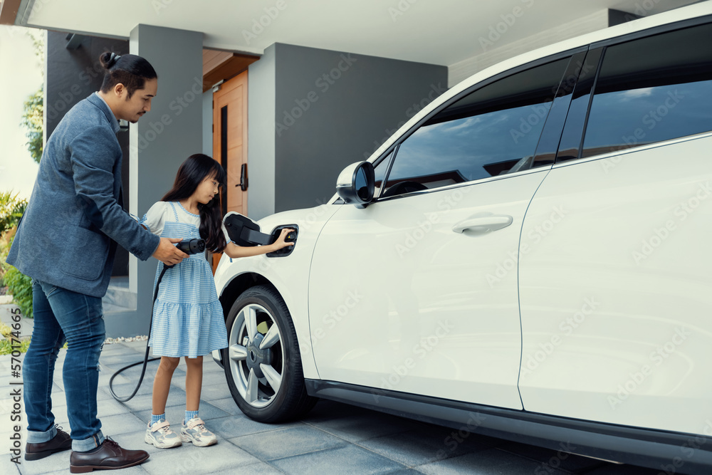 Progressive father and daughter plugs EV charger from home charging station to electric vehicle. Fut