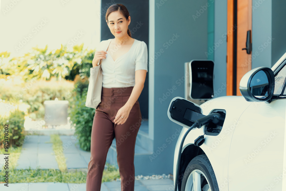 Progressive asian woman and electric car with home charging station. Concept of the use of electric 