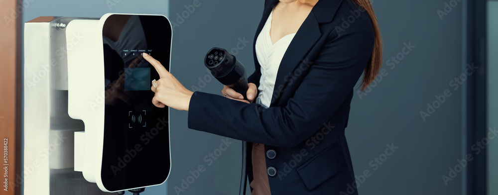 Closeup asian woman holding and pointing an EV plug, a home charging station providing a sustainable