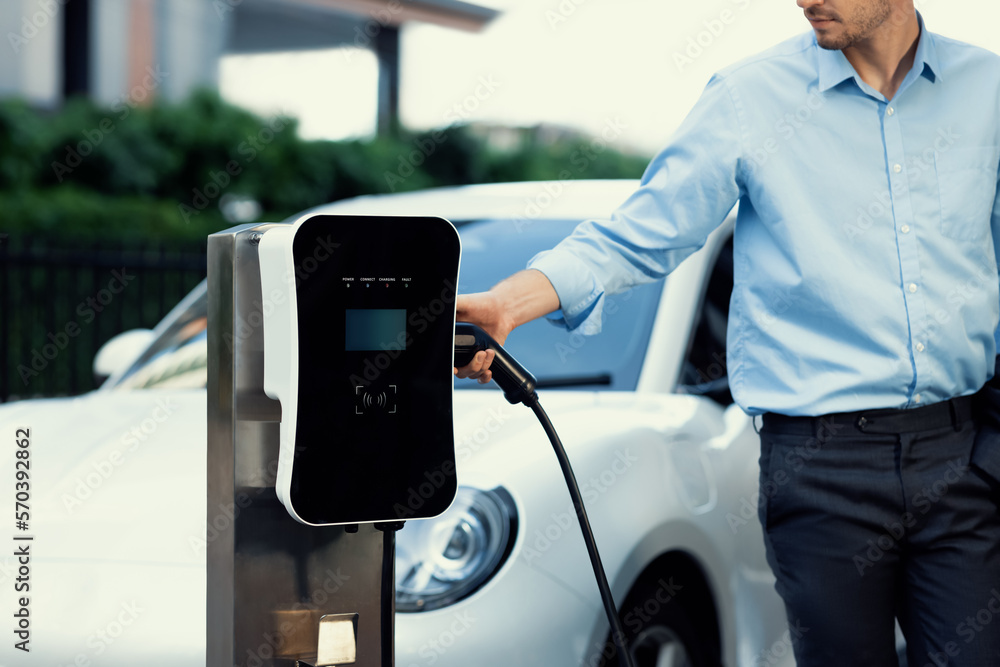 Closeup progressive man holding EV charger plug from public charging station for electric vehicle wi