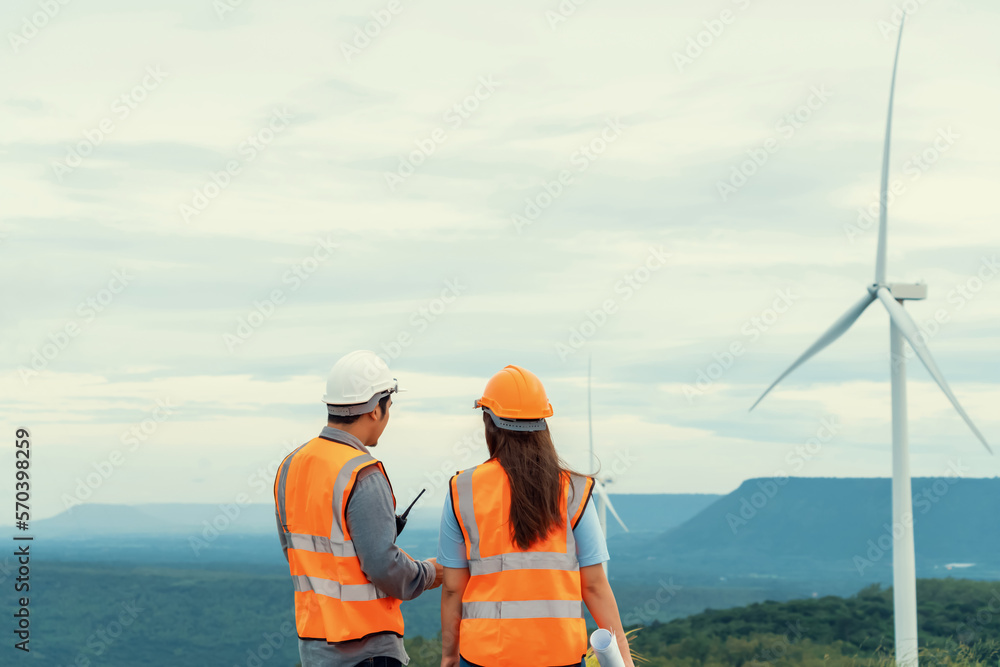 Male and female engineers working on a wind farm atop a hill or mountain in the rural. Progressive i