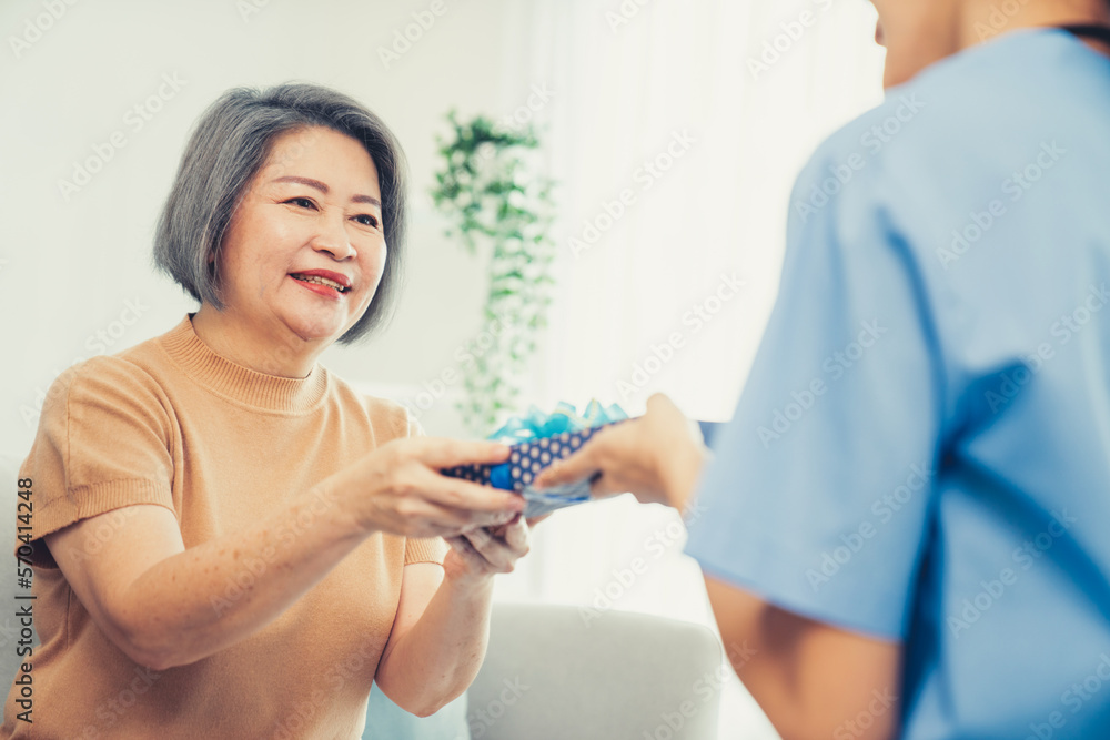 A young caregiver hand over to her senior patient a blue gift box with blue ribbons at a contented l