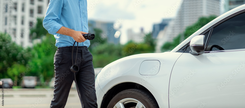 Closeup progressive man holding EV charger plug from public charging station for electric vehicle wi