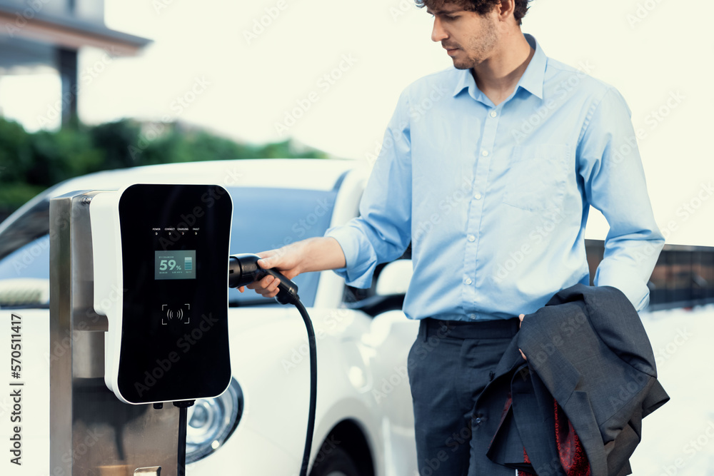 Progressive businessman insert charger plug from charging station to his electric vehicle with apart