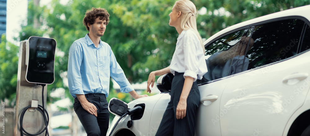 Progressive businessman and businesswoman with electric car parking and connected to public charging