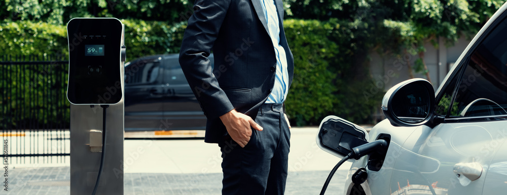 Closeup progressive suit-clad businessman with his electric vehicle recharge his car on public charg