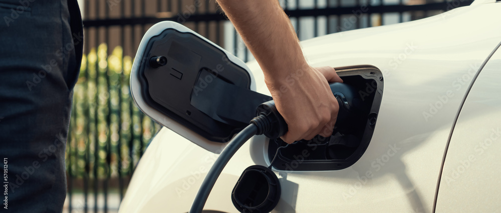 Closeup progressive man holding EV charger plug from public charging station for electric vehicle wi