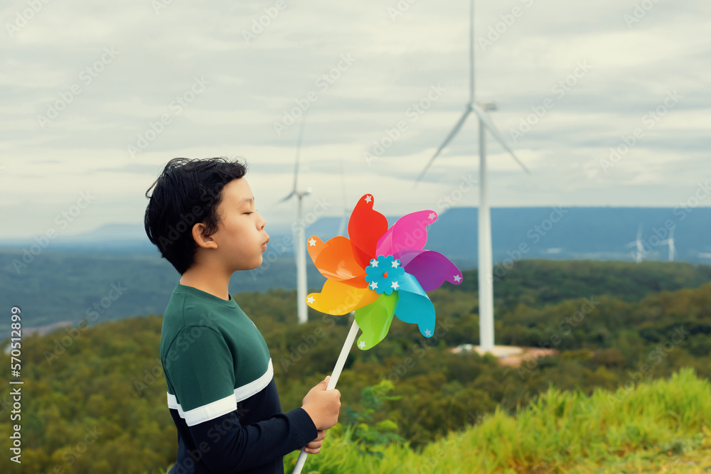 Progressive young asian boy playing with wind pinwheel toy in the wind turbine farm, green field ove