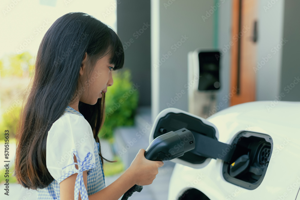 A playful girl holding an EV plug, a home charging station providing a sustainable power source for 