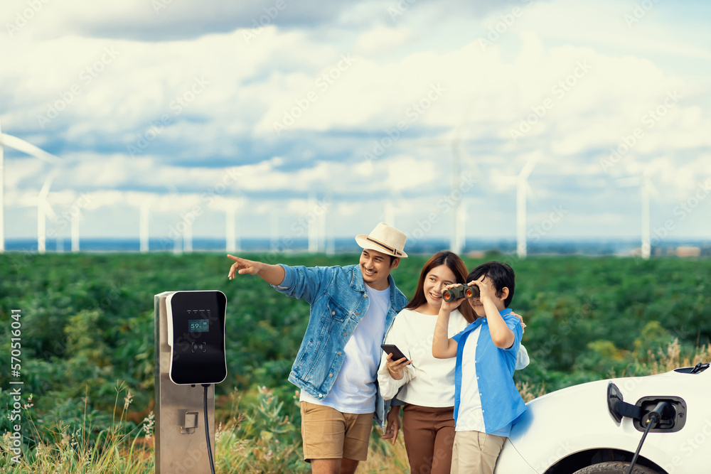 Concept of progressive happy family enjoying their time at wind farm with electric vehicle. Electric