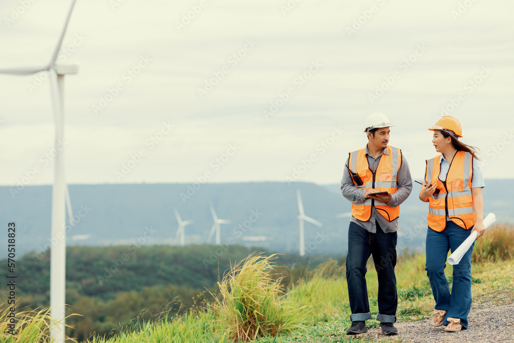 Male and female engineers working on a wind farm atop a hill or mountain in the rural. Progressive i