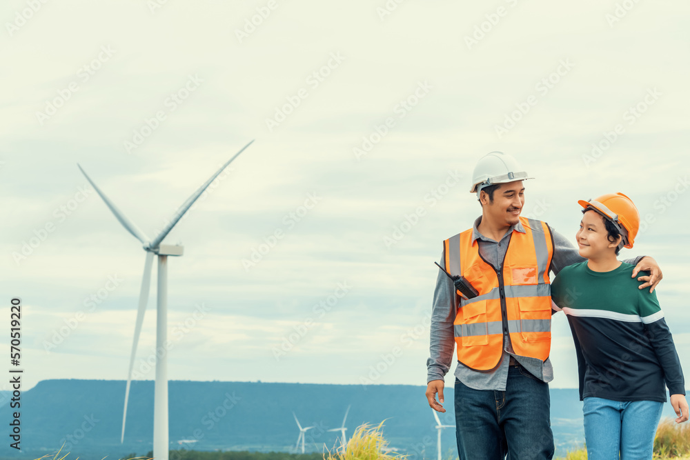 Engineer with his son on a wind farm atop a hill or mountain in the rural. Progressive ideal for the