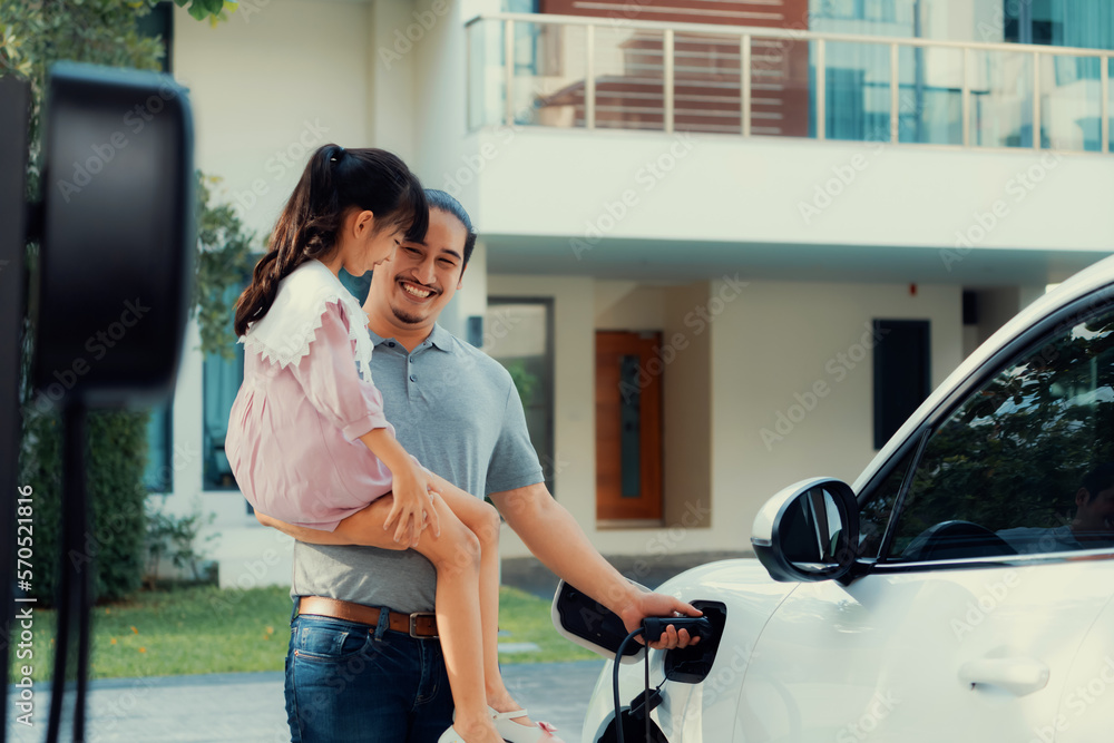 Progressive father and daughter returned from school in electric vehicle that is being charged at ho