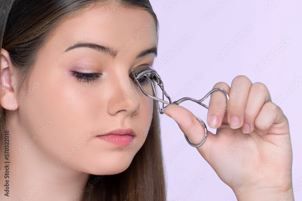 Closeup happy young charming brunette holding eyelash curler in her hand as makeup accessory. Beauti