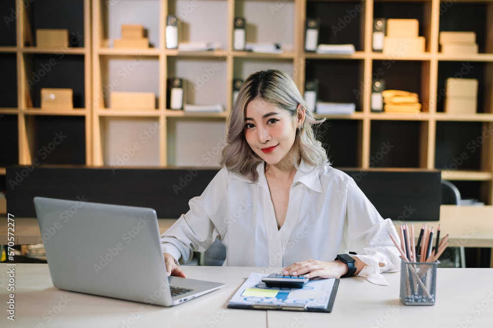 Confident beautiful Asian businesswoman typing laptop computer and digital tablet while holding coff