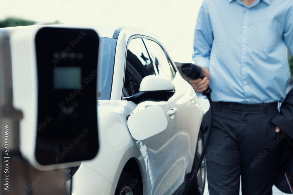 Closeup progressive suit-clad businessman with his electric vehicle recharge his car on public charg