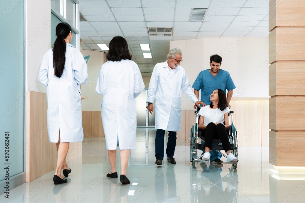 Doctor and male nurse transport a female patient in a wheelchair along sterile hospital corridor. He