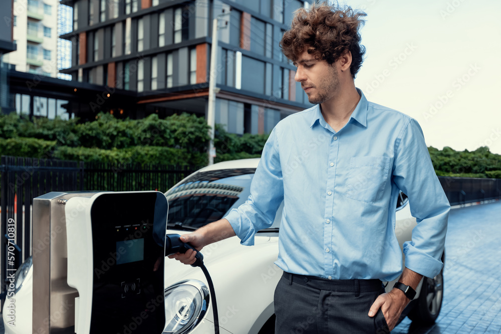 Progressive businessman insert charger plug from charging station to his electric vehicle with apart