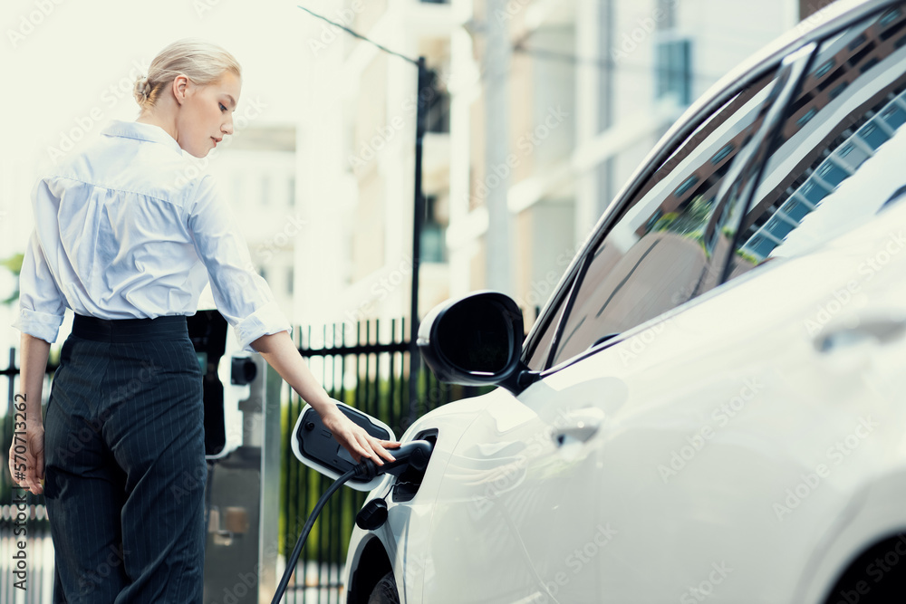 Progressive businesswoman insert charger plug from charging station to her electric vehicle with apa