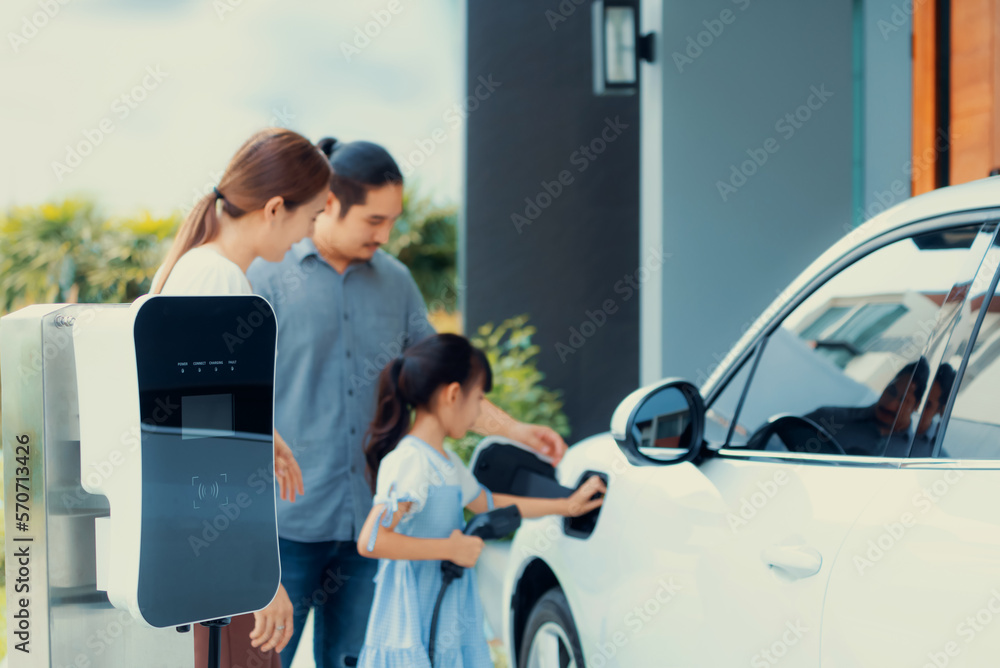 Closeup focus hand insert EV charger plug to electric vehicle at home charging station with blurred 