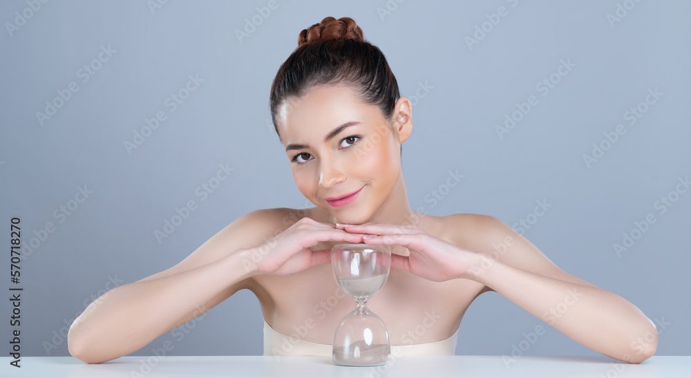 Glamorous model holding hourglass in beauty concept of anti-aging skincare treatment for woman. Youn