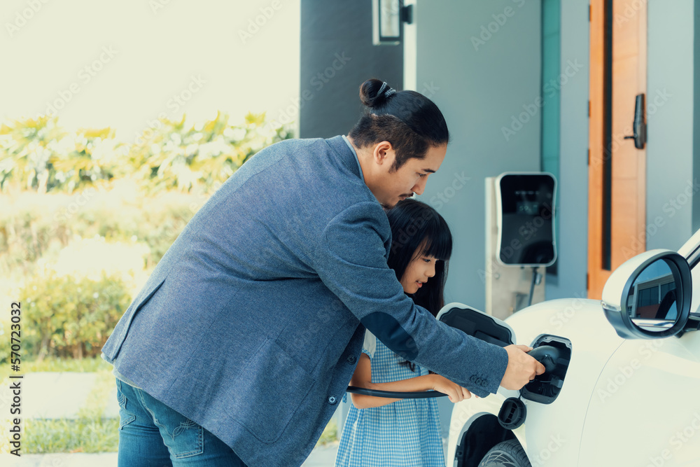 Progressive father and daughter returned from school in electric vehicle that is being charged at ho