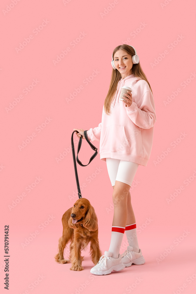 Young woman in headphones with cute cocker spaniel and cup of coffee on pink background