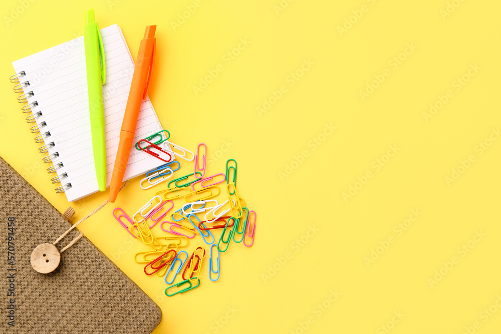 Notebooks, pens and paper clips on yellow background