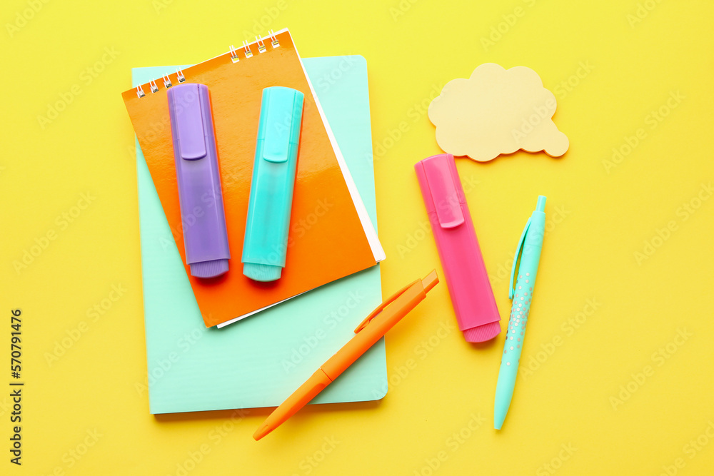 Notebooks, pens, markers and sticky notes on yellow background