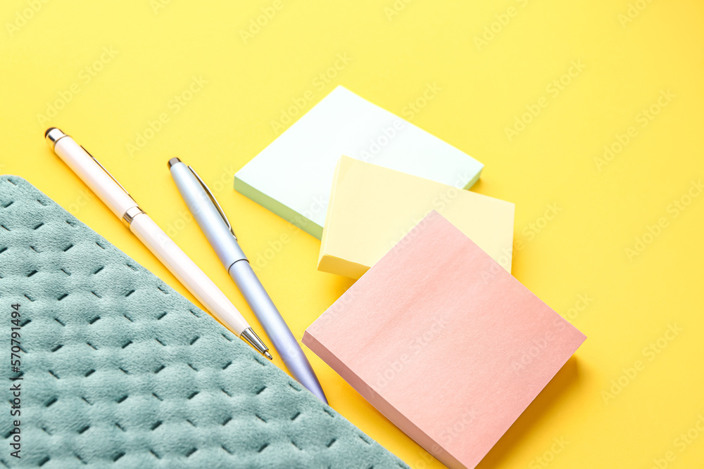 Sticky notes, pens and notebook on yellow background, closeup