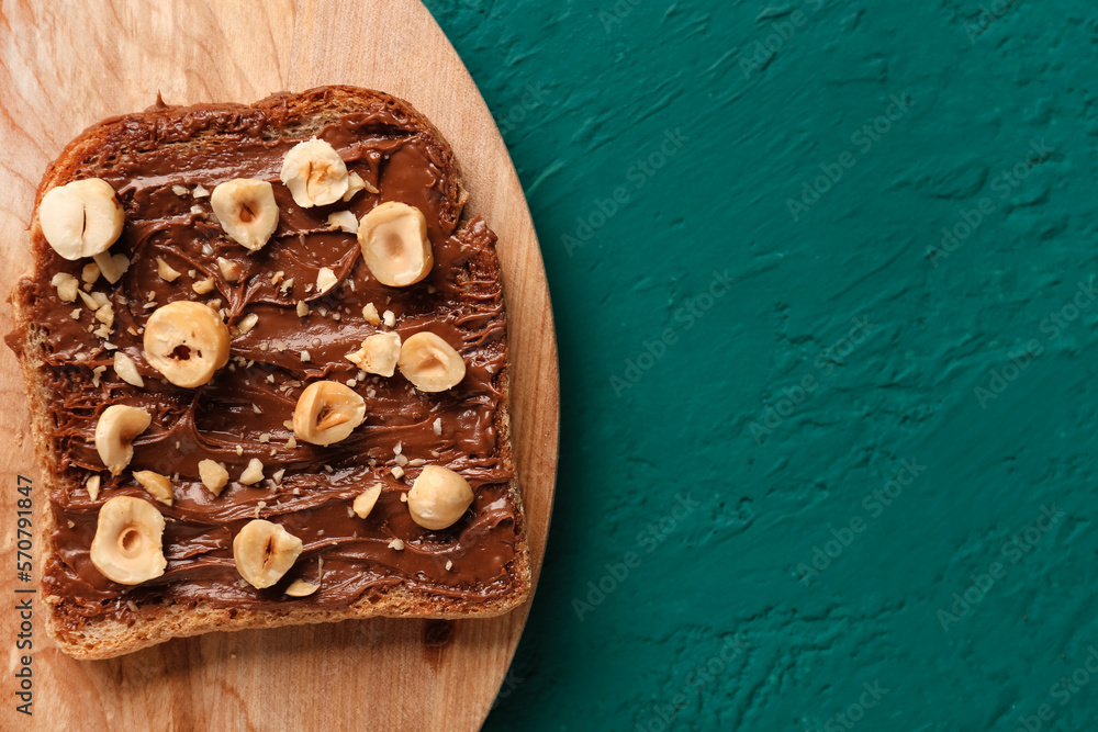 Wooden board of tasty toast with hazelnut butter and nuts on color background, closeup