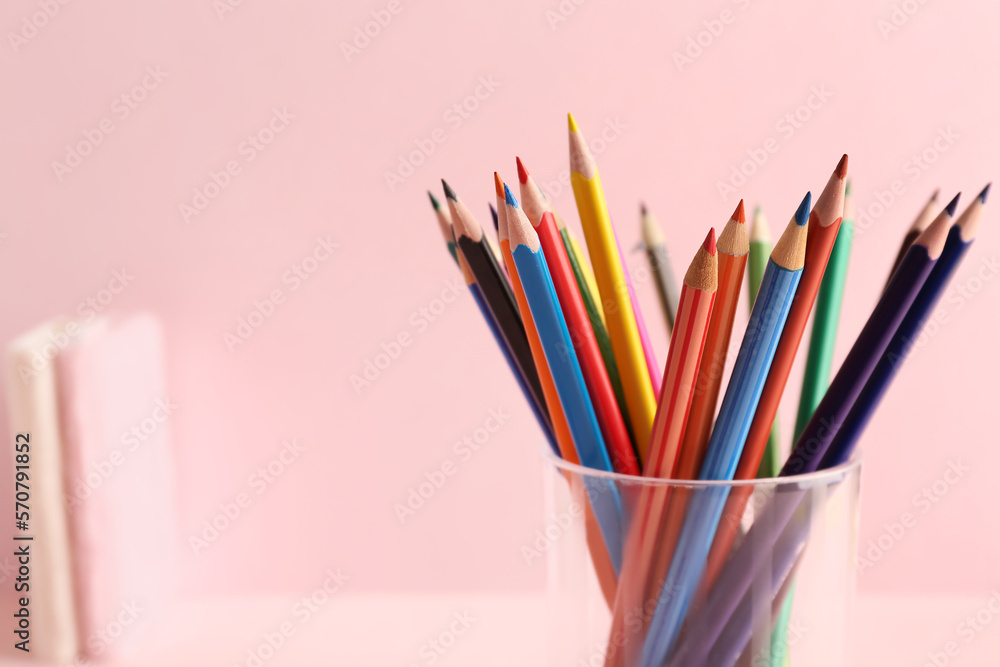 Glass with colorful pencils on pink background, closeup