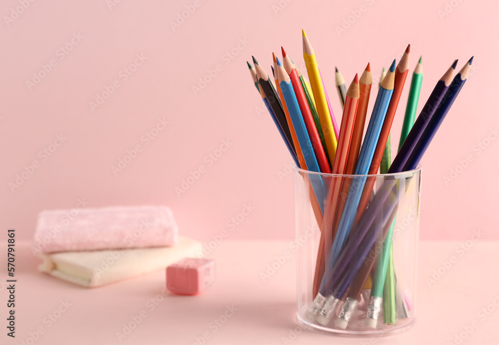 Glass with colorful pencils on pink background