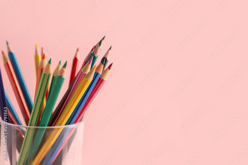 Glass with colorful pencils on pink background, closeup