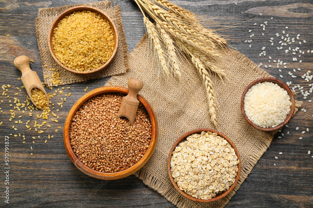 Composition with bowls of different cereals and spikelets on dark wooden background