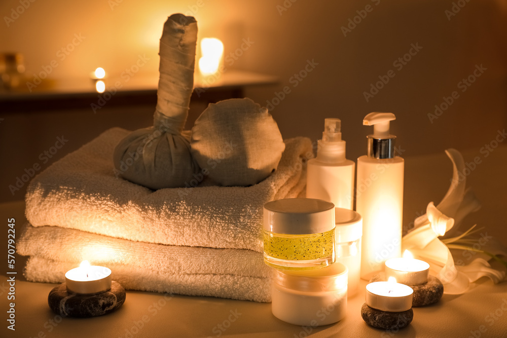 Spa composition with lily flower and burning candles on couch in dark salon, closeup