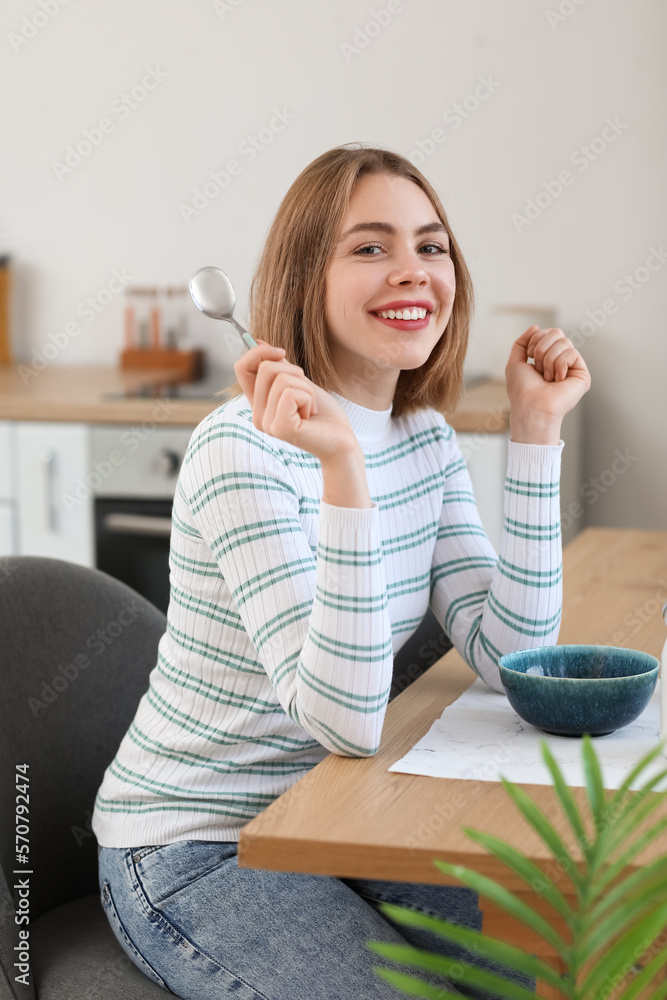 Young woman having breakfast at table in kitchen