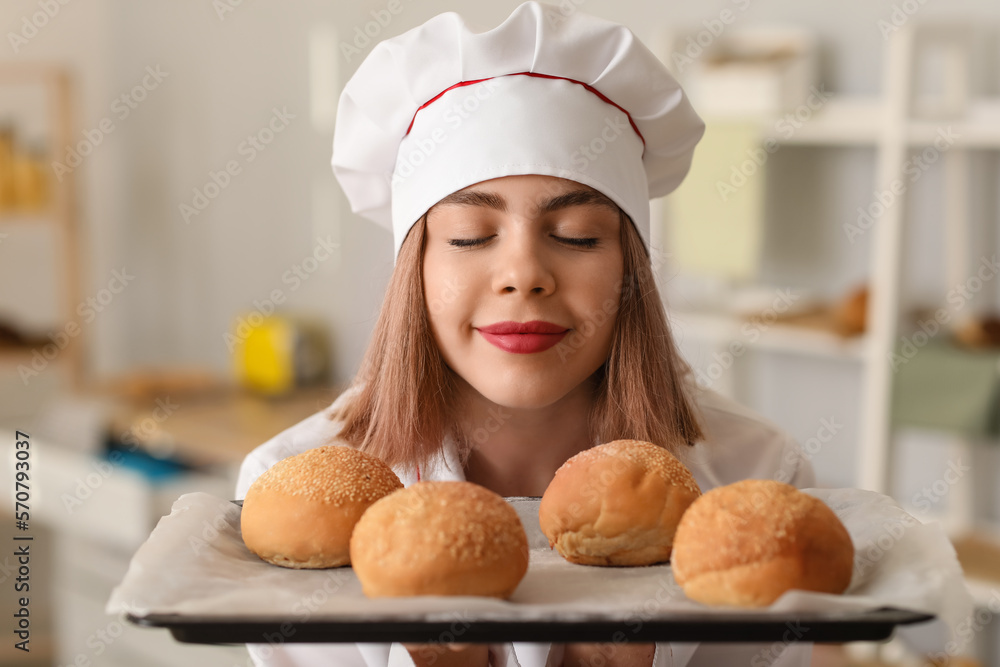 Female baker with tray of tasty buns in kitchen, closeup