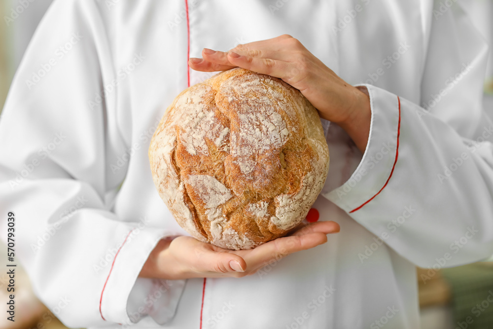 Female baker with fresh bread in kitchen, closeup