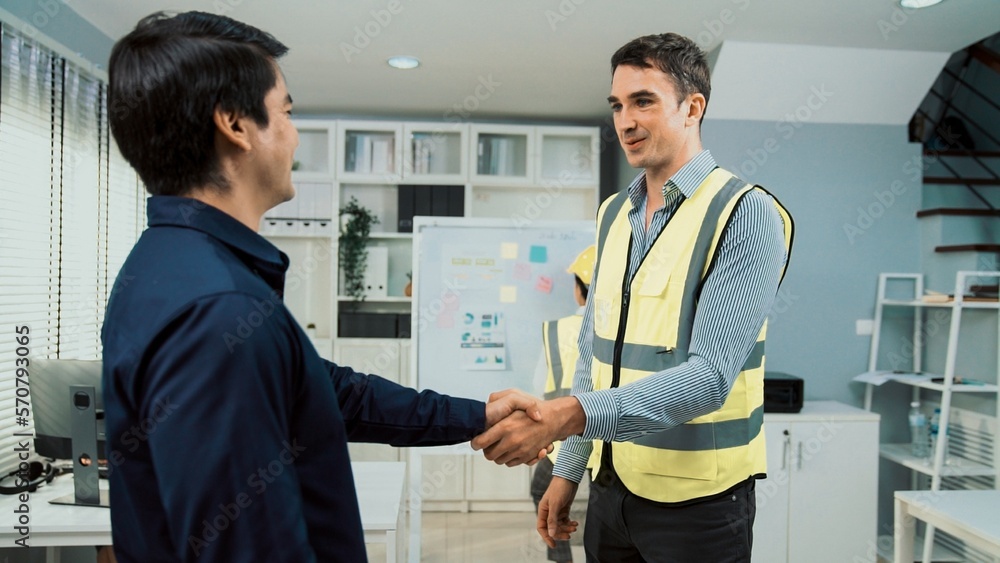 An engineer with a protective vest handshake with an investor in his office. Following a successful 