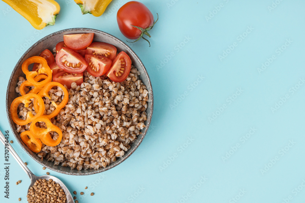 Bowl of tasty buckwheat porridge with fresh vegetables on blue background