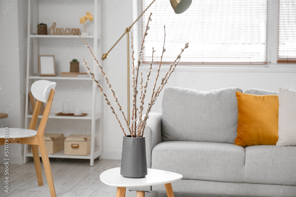 Vase with willow branches on table in light living room