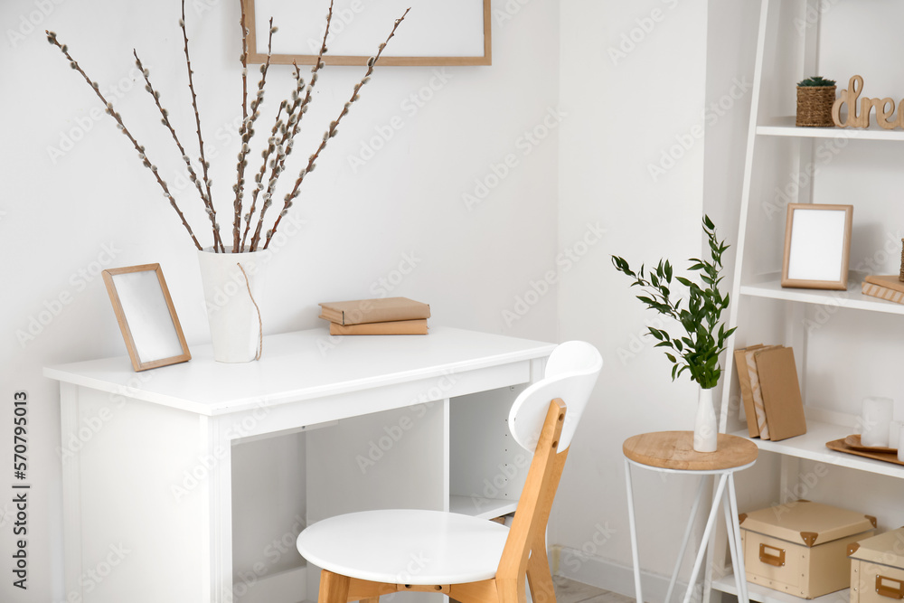 Workplace with willow branches in vase and frame near light wall