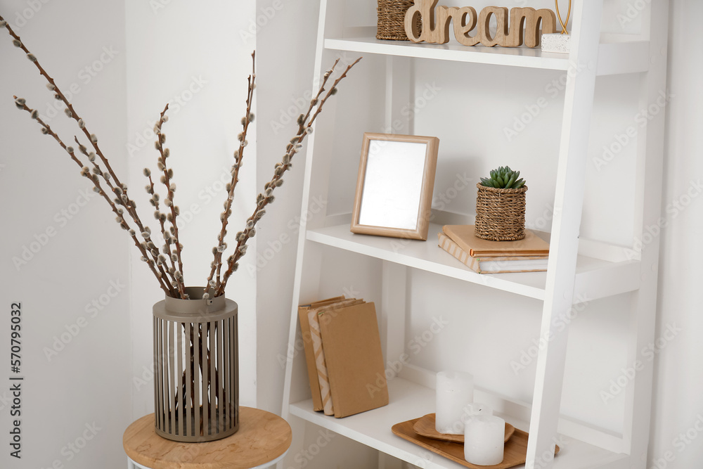 Vase with willow branches on table near shelving unit in room