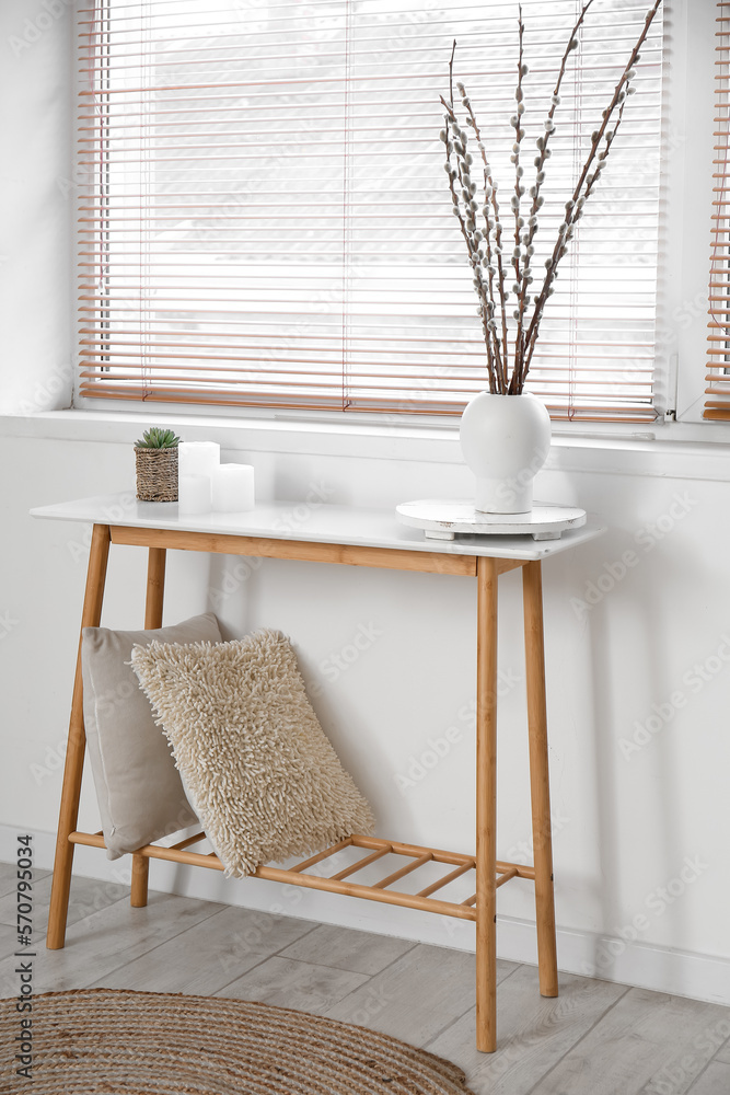 Vase with willow branches, candles and houseplant on table in light room