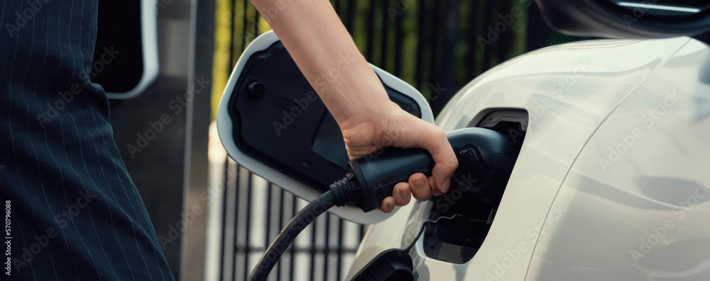 Focus EV charger plug and electric car at public charging station with blur progressive businesswoma