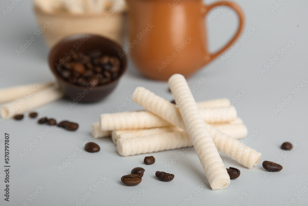 Delicious wafer rolls and coffee beans on grey background