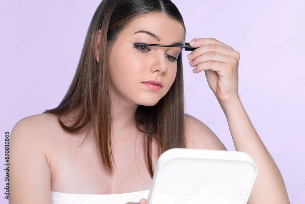 Closeup portrait of young charming applying makeup eyeshadow on her face with brush, mascara with fl